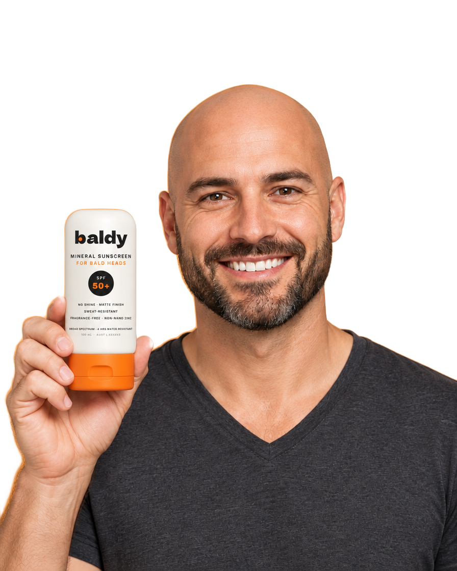 Smiling bald man holding a BALDY mineral sunscreen bottle