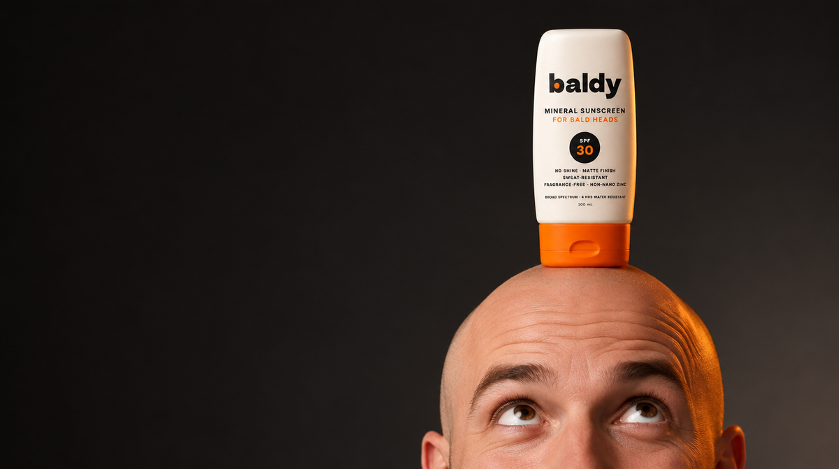 Bald man looking up with a BALDY SPF 30 sunscreen bottle balanced on his head